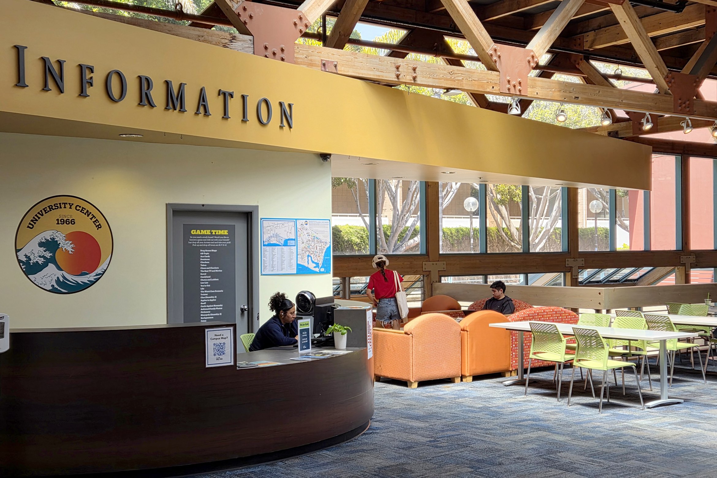 A bright university info center with seating, a help desk, large windows, and students relaxing or seeking assistance.